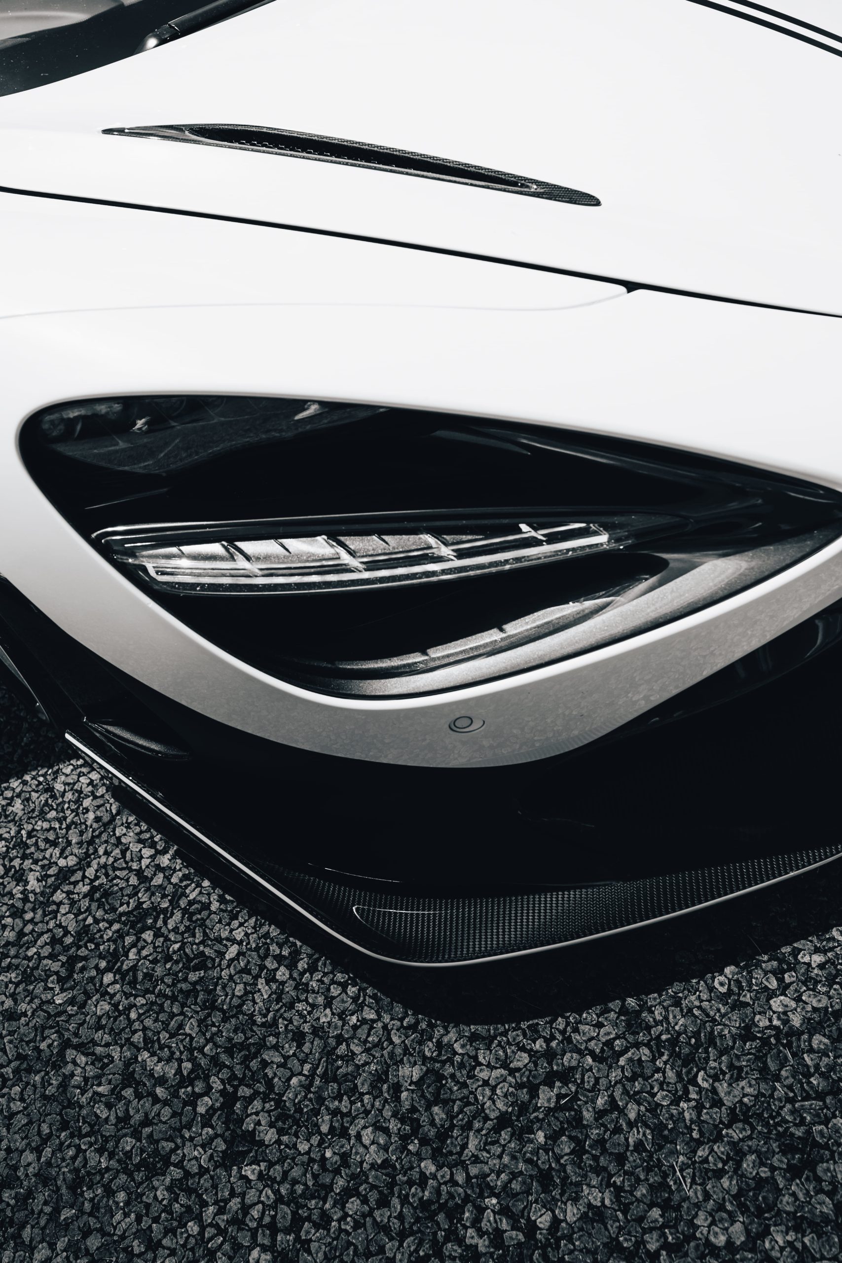 Black and white close-up of a sports car headlight and carbon fibre splitter